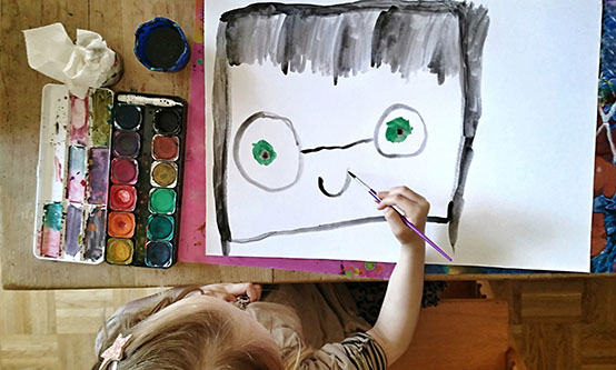Child painting smiling portrait of a face with spectacles